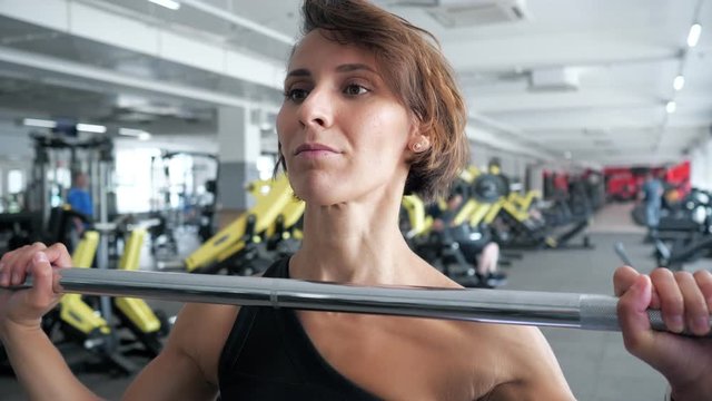 Athletic mature woman is making set of reps exercise with barbell lifting it over the head in gym. Sports workout in the gym.