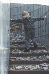 The child is alone, abandoned. Little boy on the destroyed steps of the building.