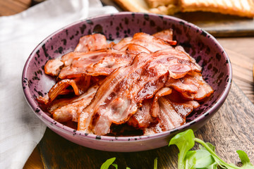 Plate with fried bacon on wooden table