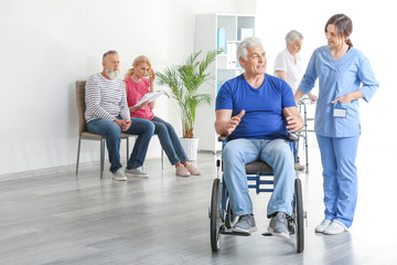 Young caregiver looking after disabled mature man in nursing home - obrazy, fototapety, plakaty