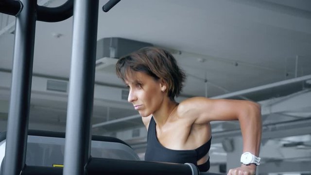 Athletic woman in sportswear is doing push-ups on parallel bars in gym, toned. Sport and bodybuilding concept, side view