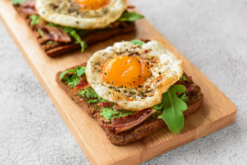 Tasty toasts with bacon and fried egg on wooden board
