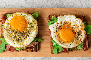 Tasty toasts with bacon and fried egg on wooden board