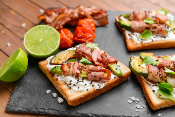 Tasty toasts with bacon on slate plate