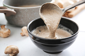 Pouring of delicious cream soup into bowl on table