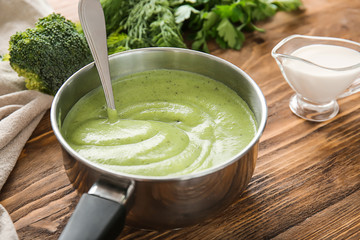 Saucepan with delicious broccoli cream soup on wooden table