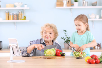Cute little girl with grandmother preparing vegetable salad in kitchen