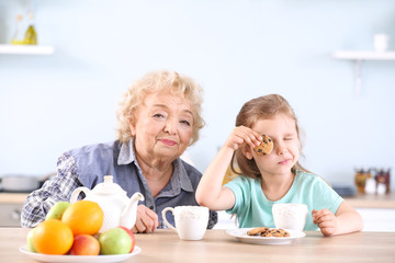 Cute little girl and grandmother drinking tea with cookies in kitchen