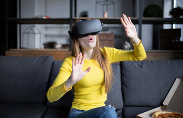 Beautiful woman touching air during the VR experience. Girl eats pizza