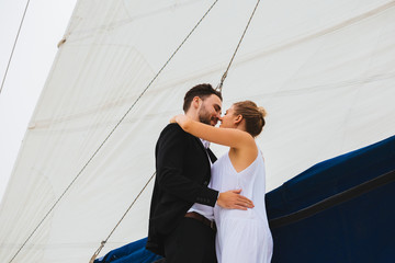 Handsome man and attractive woman smiling and kissing embracing on yacht in bright day