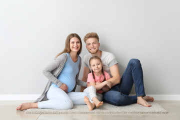 Beautiful pregnant woman with her family sitting near light wall