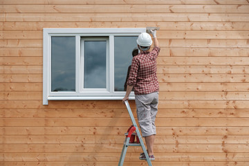 a young woman paints the outside wall of a new wooden house. the process of painting a country house