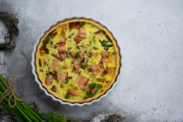 Baked Lauren quiche with bacon and young bracken shoots on white background with birch bark. Top view