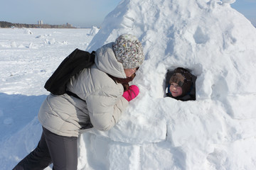 Woman in a light jacket talking to a boy sitting in an igloo