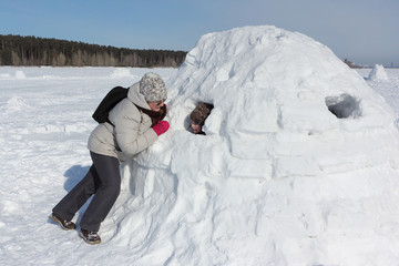 Woman in a light jacket talking to a boy sitting in an igloo