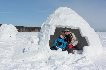 Happy grandmother and grandson sitting in an igloo on a snowy glade in winter, Novosibirsk, Russia