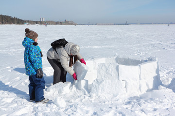 Happy grandmother and grandson building an igloo on a snowy glade in winter, Novosibirsk, Russia