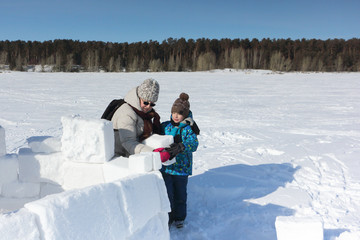 Happy grandmother and grandson building an igloo on a snowy glade in winter, Novosibirsk, Russia