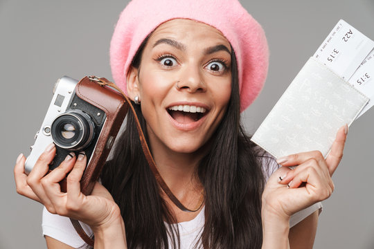 Photo closeup of amazed pretty tourist woman in beret laughing while holding retro camera and travel tickets