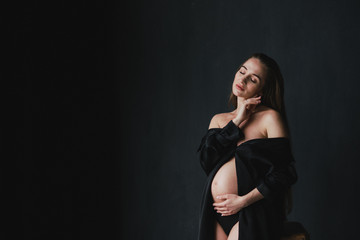 Pregnant caucasian long-haired woman in a beautiful dress holding her hands on her belly....