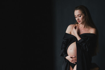 Pregnant caucasian long-haired woman in a beautiful dress holding her hands on her belly. Pregnancy, happiness, expectation concept.