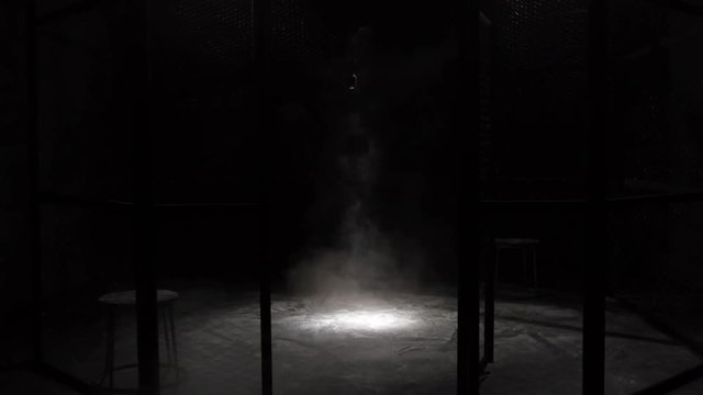 White smoke Projection in a metal grilles cage, circular MMA boxing ring, in a dark studio with a Spotlight or light shower. Show with Vintage microphone. Tracking out. Smoke coming from the ground.