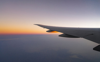 Wing of plane over the city. Airplane flying on blue sky. Scenic view from airplane window. Commercial airline flight in the morning with sunlight. Plane wing above clouds. Flight mechanics concept.