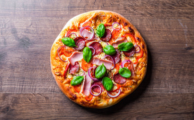 Pizza with Mozzarella cheese, ham, tomato sauce, salami, onion, pepper, Spices and Fresh basil. Italian pizza on wooden table background