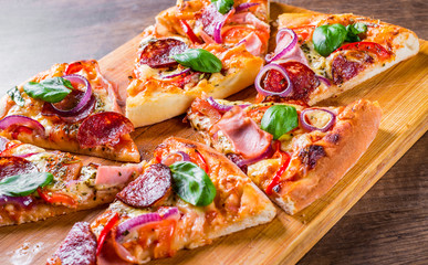 Pizza with Mozzarella cheese, ham, tomato sauce, salami, onion, pepper, Spices and Fresh basil. Italian pizza on wooden table background
