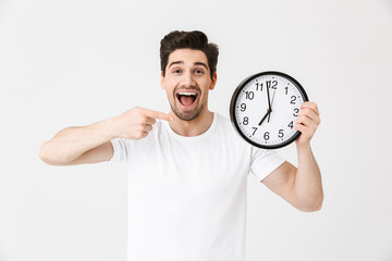 Shocked excited happy young man posing isolated over white wall background holding clock.