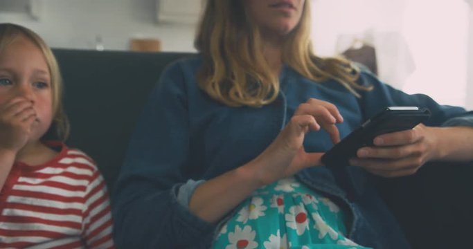 Mother using smartphone with toddler watching television
