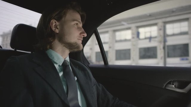 man with brown hair in pistachio shirt and grey suit riding in car and looking around