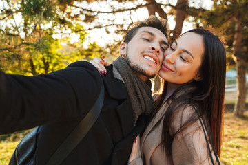 Happy young beautiful loving couple posing walking outdoors in park nature take selfie by camera.