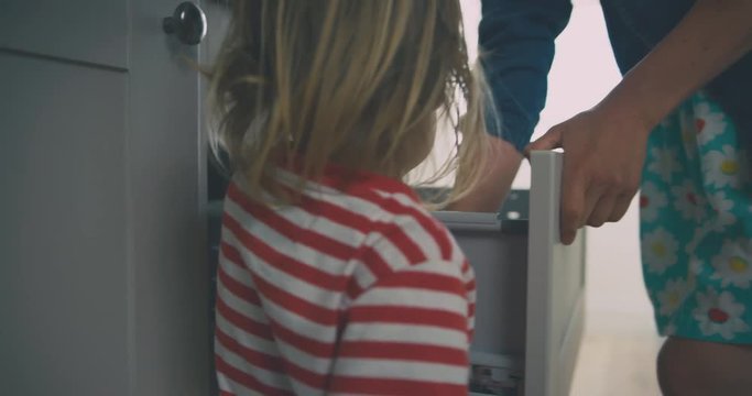 Young mother and toddler getting spoon from drawer