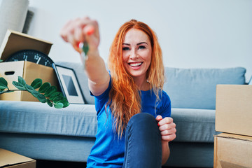Cheerful young woman looking at camera and showing keys to new apartment