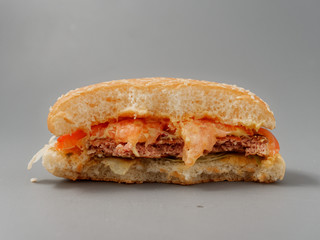 bitten big burger with cutlet cheese and tomato on a gray background