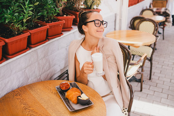Young beautiful woman in glasses having french breakfast in cafe