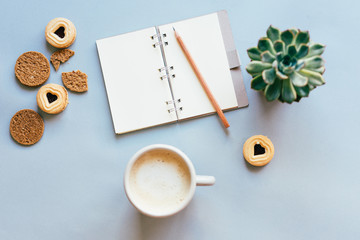 Top view of a cozy composition with a cup of coffee and cookies and a notepad for writing.