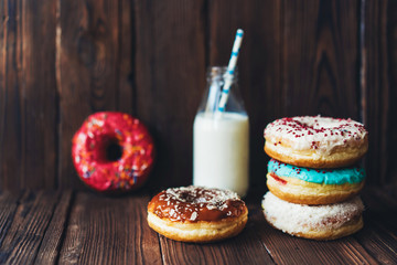 A group of delicious sweet covered colored donut glaze and a bottle of milk on a dark wooden...