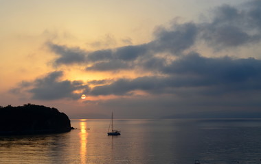 Seascape, lonely yacht. Setting sun in the clouds