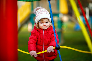 Cute toddler girl having fun on playground. Happy healthy little child climbing, swinging and...