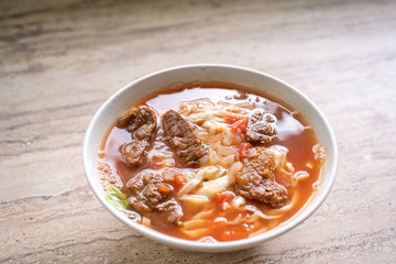 Beef noodle ramen meal with tomato sauce broth in bowl on bright wooden table, famous chinese style food in Taiwan, close up, top view, copy space