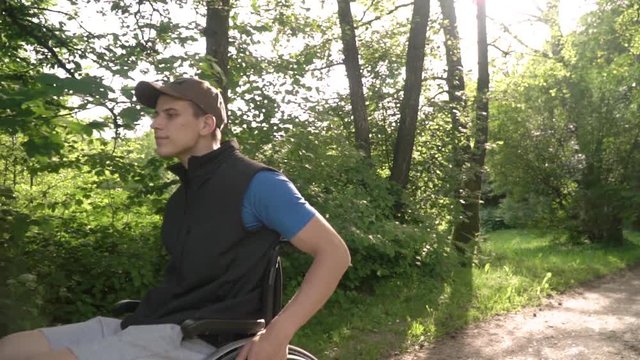 Slowmotion follow of disabled young student man in a wheelchair observing nature around him, with sun flare