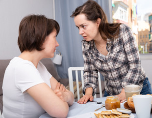 Upset adult woman quarrel with female friend at table with cookies