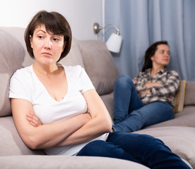 Mature female  sitting at sofa after quarrel quarrel, woman on background