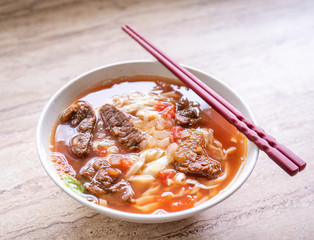 Beef noodle ramen meal with tomato sauce broth in bowl on bright wooden table, famous chinese style food in Taiwan, close up, top view, copy space