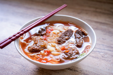 Beef noodle ramen meal with tomato sauce broth in bowl on bright wooden table, famous chinese style food in Taiwan, close up, top view, copy space