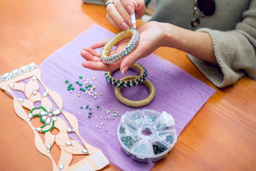Close-up woman`s hands, decorating bracelets with colorful shiny rhinestones, gluing crystals on a...