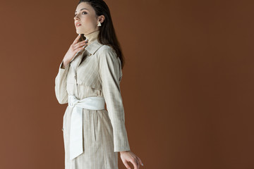 stylish woman in trendy trench coat isolated on brown, looking away