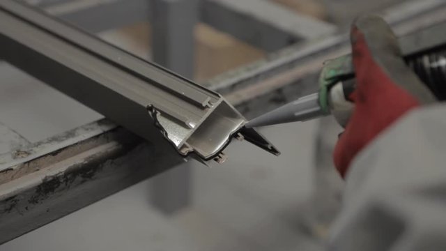 Worker applying black silicone sealing with caulking gun for moisture protection on window, processing of aluminum parts in a Production of aluminium Windows Workshop. Manufacturing of windows.